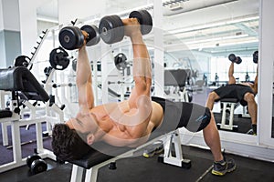 Muscular man exercising with dumbbells in gym