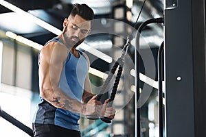 Muscular man exercising with training apparatus in gym