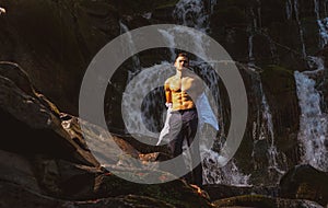 muscular man going to swim in waterfall water. Profit business concept. businessman undressing at waterfall ready to