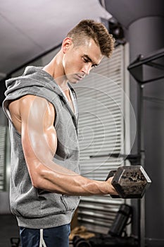 Muscular man with grey jumper lifting dumbbell