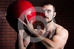 Muscular man in the gym lifting a red ball