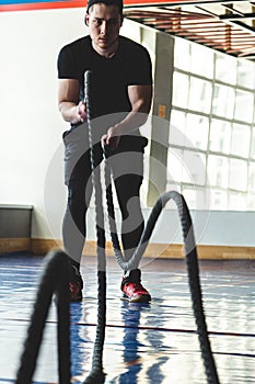 Muscular man in the gym with ropes doing exercises. Crossfit