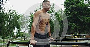 Muscular man has workout, pull up and raise knees on parallel bar outdoors