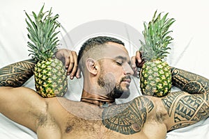 Muscular man hold pineapple fruit on biceps. brutal sportsman relax in bed. steroids. sexy ab of tattoo man diet. male photo