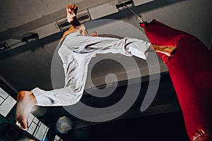 Muscular man kick boxing with red punching bag at gym