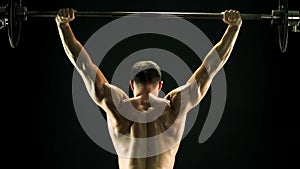 Muscular man lifting barbell, back view.