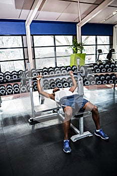 Muscular man lifting barebell while lying on bench