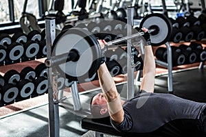 Muscular man lifting barebell while lying on bench