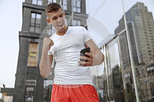 Muscular man looking at his smartphone outside