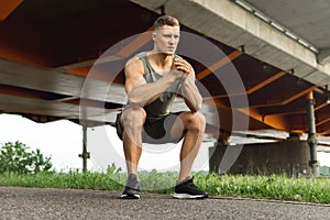 Muscular man is making squats under the bridge during his street workout