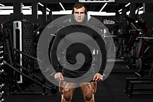 Muscular man with muscle legs in gym. Strong male in black hoodie with big quads photo