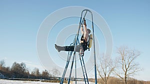 Muscular man with a naked torso is training in a winter park and doing exercise corner and plank on a horizontal bar