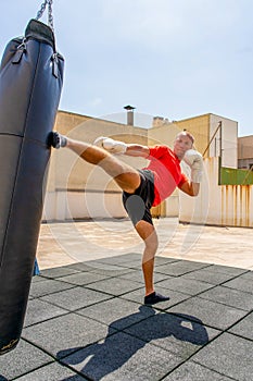 Muscular man punching with leg a boxing bag on cross fit training at the outdoors. Training concept