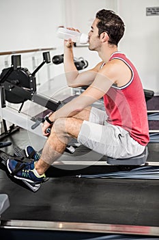 Muscular man on rowing machine drinking water