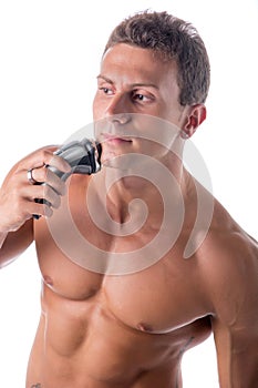 Muscular man shirtless using electric shaver, looking away