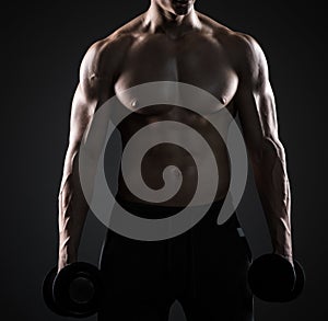 Muscular man showing perfect body with dumbbells on black background