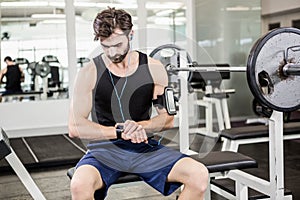 Muscular man sitting on barbell bench and using smartwatch