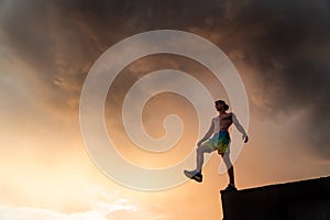 Muscular man stepping from the edge during dramatic sunset. Concept of choice and courage