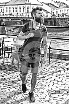 Muscular man with stylish beard and mustache carrying big sporty bag while walking in old city. Young man in denim short