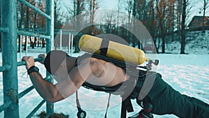 Muscular man without a t-shirt with a ballon compressed air drager on his back is training in a winter park and doing