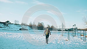 A muscular man without a T-shirt with a drager on his back goes through the snow to the horizontal bars. Back view