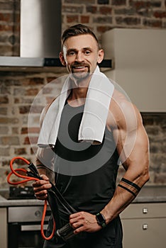 A muscular man with a towel on the shoulders is posing with pull elastic rope