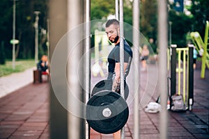 Muscular man training in park. Heavy weight lifting in park with dumbells