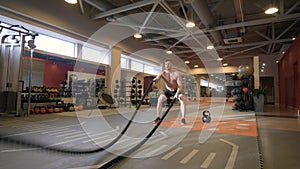 Muscular man training workout exercise with ropes in fitness club