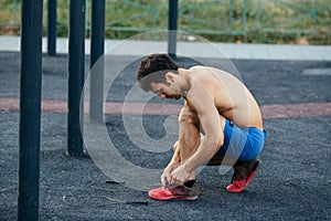 Muscular man tying shoes before exercise at crossfit ground, closeup. Sport concept