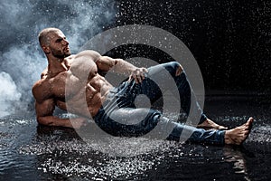 Muscular man under the rain in studio. Sexy male in water drops, abs