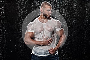 Muscular man under the rain in studio. Sexy male in water drops