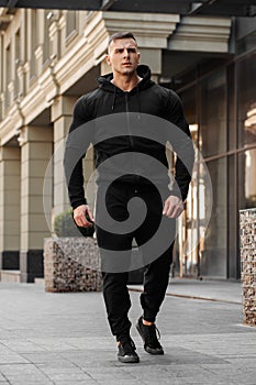 Muscular man wears black sportswear on the street. Athletic male outdoors