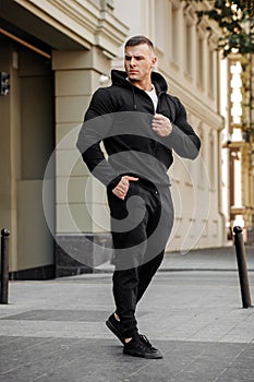 Muscular man wears black sportswear on the street. Athletic male outdoors