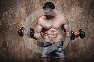 Muscular man working out with dumbbells on wall background