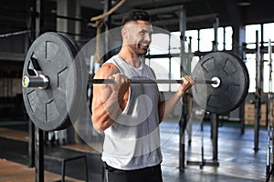 Muscular man working out in gym doing exercises with barbell at biceps