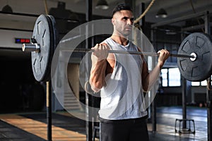 Muscular man working out in gym doing exercises with barbell at biceps