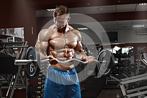 Muscular man working out in gym doing exercises with barbell at biceps, male naked torso abs