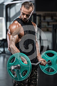 Muscular man working out in gym doing exercises with barbell at biceps, strong male bodybuilder