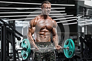 Muscular man working out in gym doing exercises with barbell at biceps, strong male naked torso abs