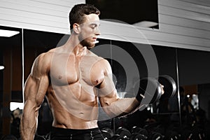 Muscular man working out in gym doing exercises with dumbbells