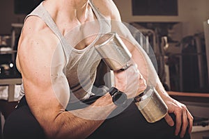 Muscular man working out in gym doing exercises with dumbbells at biceps