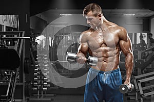 Muscular man working out in gym doing exercises with dumbbells at biceps, strong male naked torso abs