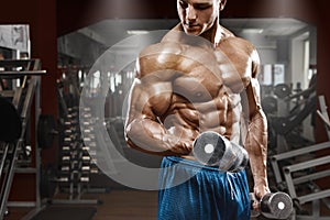 Muscular man working out in gym doing exercises with dumbbells at biceps, strong male naked torso abs