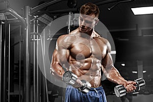 Muscular man working out in gym doing exercises with dumbbells at biceps, strong male naked torso abs