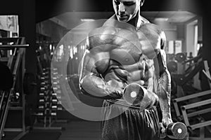 Muscular man working out in gym doing exercises with dumbbells at biceps, strong male torso abs