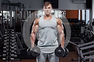 Muscular man working out in gym doing exercises with dumbbells, strong male