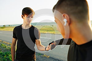 Muscular men clapping hands and preparing for workout an a field. Both listen to music on wireless headphones and wear a