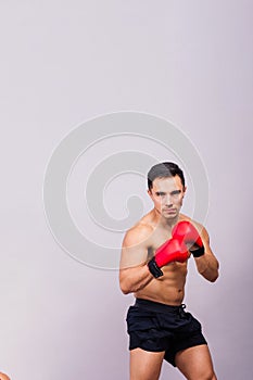 Muscular model sports young man in boxing gloves on grey background. Male flexing his muscles