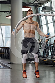 Muscular powerful aggressive man training with rope in functional training fitness gym. Motion blur