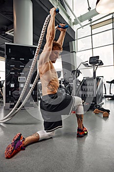 Muscular powerful aggressive man training with rope in functional training fitness gym. Motion blur